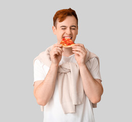 Young man eating piece of tasty pizza on white background