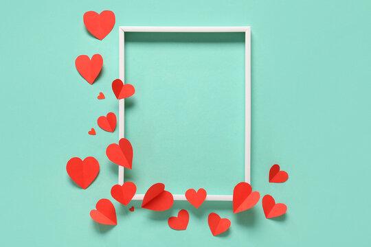 Composition with empty picture frame and red paper hearts on color background. Valentines Day celebration