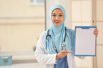 Female Muslim doctor in hijab with clipboard at clinic. World Hijab Day concept