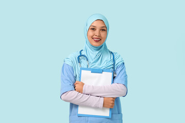 Female Muslim doctor in hijab with clipboard on blue background. World Hijab Day concept