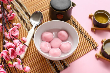 Bamboo mat with bowl of tangyuan, tea and sakura on pink background, closeup. Dongzhi Festival
