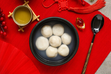 Bowl of tangyuan, tea and Chinese decor on red mat, closeup. Dongzhi Festival