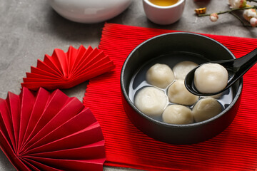 Red mat with bowl of tangyuan and Chinese decor on grey grunge background, closeup. Dongzhi Festival