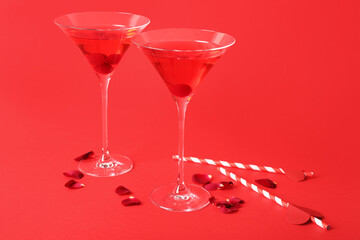 Glasses of tasty cocktail with straws and rose petals on red background. Valentine's Day celebration