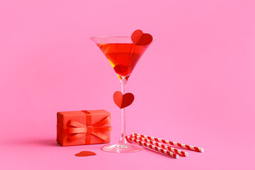 Glass of tasty cocktail with straws and gift on pink background. Valentine's Day celebration