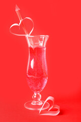 Glass of tasty cocktail with straw on red background. Valentine's Day celebration
