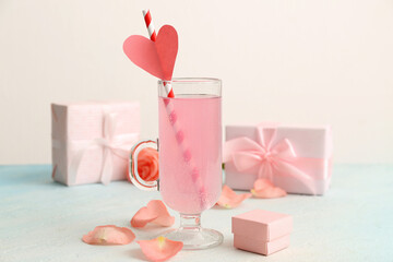 Glass of tasty cocktail with ring box and rose petals on blue grunge table against white background. Valentine's Day celebration
