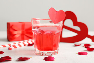 Glass of tasty cocktail with rose petals on white background. Valentine's Day celebration