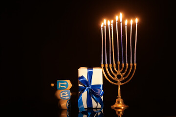 Menorah with burning candles, dreidels and gift for Hanukkah celebration on dark background