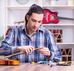Young handsome repairman repairing violin