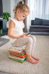 Little girl sits on a stack of children's fairy-tale books and plays the app on her smartphone