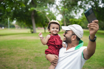 Beautiful Young indian father wearing hat and sunglasses dancing with his baby girl in the park or...
