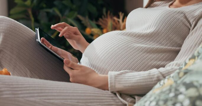 Close-up shot of a pregnant woman's hands holding a tablet, swiping and scrolling through photos with a thoughtful expression.