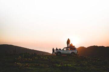 Group of travelers tourist stand by 4wd vehicle together in nature on adventure watch sunset over horizon over cloudscape in wilderness. Exploration and adventure © Evaldas