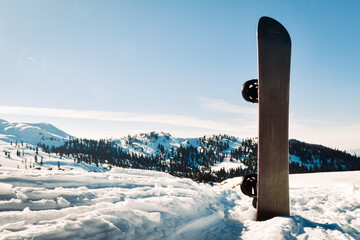 Black base snowboard in a snow with white mountains in the background. Concept of end beginning of...