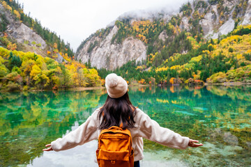 Young female tourist looking at beautiful autumn scenery landscape at jiuzhaigou national park in Sichuan, China - obrazy, fototapety, plakaty