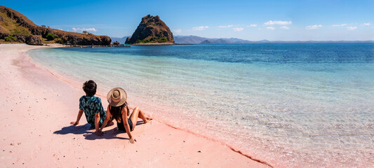 Young couple tourism enjoying the tropical pink sandy beach with clear turquoise water at Komodo islands in Indonesia - obrazy, fototapety, plakaty