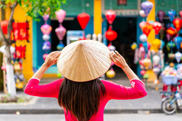 Young female tourist in Vietnamese traditional dress looking at a souvenir shop in Hoi An Ancient...