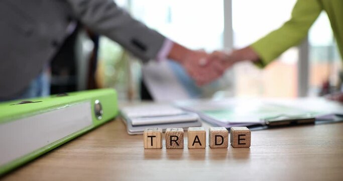 Words trade on wooden cubes on background of business people handshake 4k movie slow motion. Business deal concept