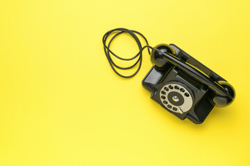 A retro black telephone on a yellow background. The old technique.