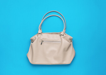 Stylish beige women's handbag on a light blue background.