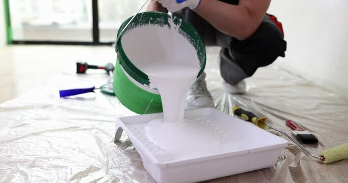 Male repairman pouring white paint from bucket into pallet closeup 4k movie slow motion. Painting works repair of apartments and houses concept