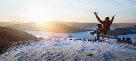 happy man traveler blogger work remote on laptop while enjoying winter nature landscape at sunset. ...