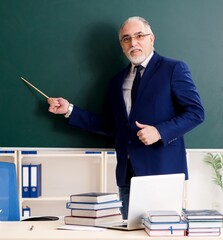 Aged male teacher in front of chalkboard