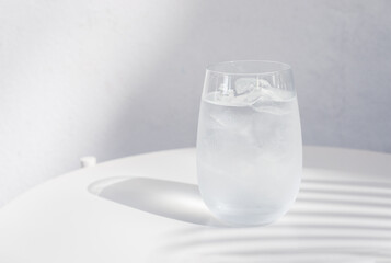a glass of water with ice on white table.