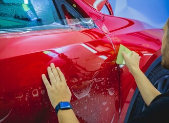 The process of installing protective film on the new red car.