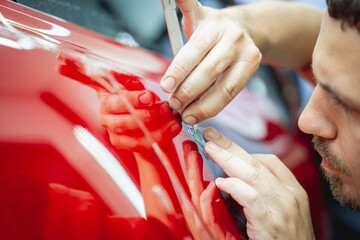 The process of installing protective film on the new red car. - obrazy, fototapety, plakaty