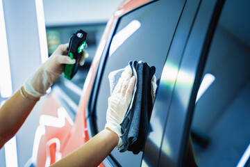 Car detailing worker cleaning and polishing car with microfiber cloth and vacuum.