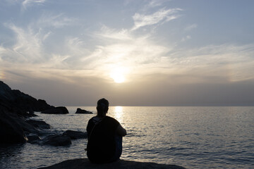 Back view of a woman relaxing by the sea with rocks coast at sunset.