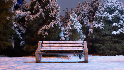 There is snowfall in the city park. The trees are covered in snow, creating a winter wonderland. You can find a snow-covered park bench in this beautiful setting.