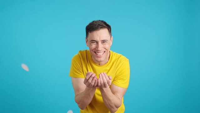 Smiling man blowing confetti on blue chroma key background