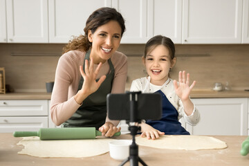 Family cooking blogger mom and happy cute kid girl in aprons baking in home kitchen together,...