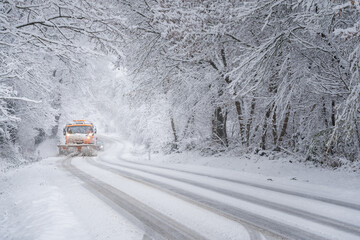 A snowy landscape. A car is clearing snow from the road. 