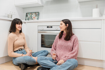 Young women gossiping while having rose champagne in kitchen