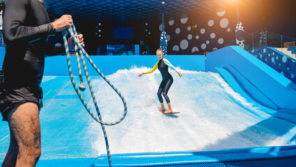 Beautiful young woman surfing with trainer on a wave simulator at a water amusement park - obrazy, fototapety, plakaty