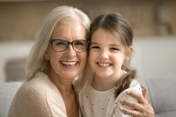 Cheerful beautiful senior grandmother and happy little granddaughter home family portrait. Positive...