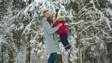 Fototapeta na wymiar Adult mother in cyan jacket plays with toddler daughter in quiet winter forest
