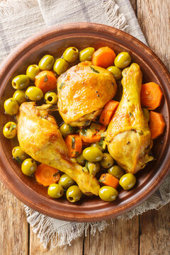 Tajine zitoune is a traditional Algerian dish made with a combination of chicken pieces, olives, onions, carrots, thyme, lemon juice, and saffron close-up on wooden table. Vertical top view from above