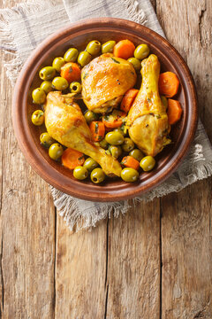 Traditional Algerian Meal Tajine Zitoune of chicken, carrots and green olives close-up on wooden table. Vertical top view from above