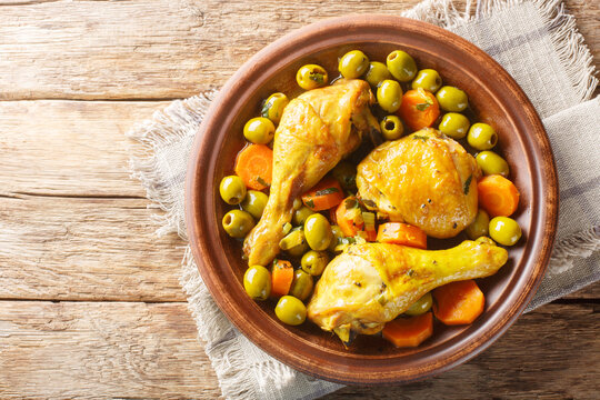 Tajine zitoun is a traditional Algerian dish made with a combination of chicken pieces, olives, onions, carrots close-up on wooden table. Horizontal top view from above