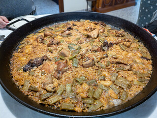Beautiful and tasty typical Valencian paella made at home, the best-known dish in Spain, on a table and you can see a person placing the plates to eat, typical Spanish tapas