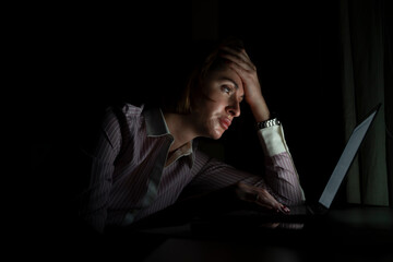 Side view of young tired businesswoman working on laptop at night. Work from home concept