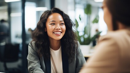 A young Asian woman with long hair smiles while sitting in an office during a meeting. - obrazy, fototapety, plakaty