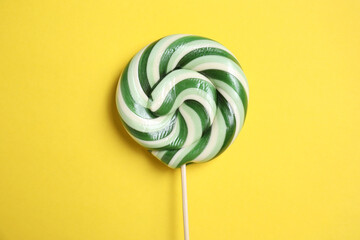 Stick with colorful lollipop swirl on yellow background, top view