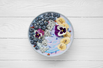 Delicious smoothie bowl with fresh fruits, blueberries and flowers on white wooden table, top view
