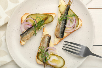 Delicious sandwiches with sprats, pickled cucumber, onion and dill served on white wooden table, top view